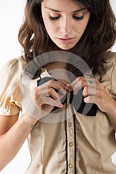 An innocent young girl unbuttons her brown shirt with bows