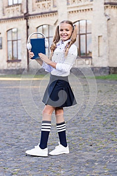 Innovative lifelong learning. using headset technology. small happy girl listen e-book. pupil in retro uniform listen