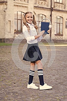 Innovative lifelong learning. using headset technology. small happy girl listen e-book. pupil in retro uniform listen