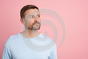 Inquisitive interested young man involved looks side on space for advertising on pink studio wall