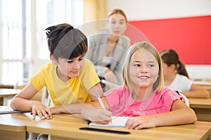 Inquisitive preteen boy peeking at workbook of cute smiling girl in class