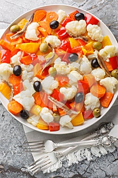 Insalata Di Rinforzo Italian cauliflower salad with giardiniera, olives and anchovies closeup on the plate. Vertical top view