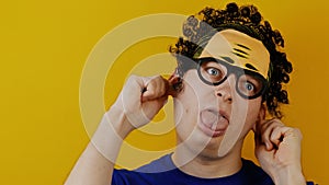 Insane curly man pulls himself by the ears and shows his tongue, funny cheerfully, human emotions, on yellow wall