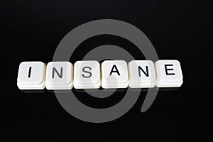 Insane text word title caption label cover backdrop background. Alphabet letter toy blocks on black reflective background. White a