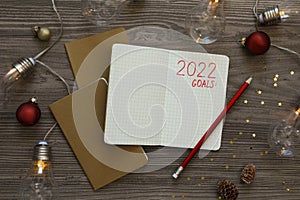 Inscription 2022 Goals written in planner and Christmas decor on wooden background, flat lay. New Year aims