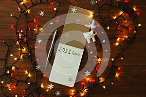 Inscription 2022 Goals written in planner and Christmas decor on wooden background, flat lay. New Year aims