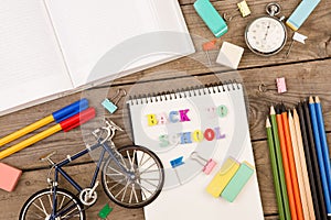 inscription of & x22;back to school& x22;, bicycle model, stopwatch, book, notepad and other stationery on brown wooden table