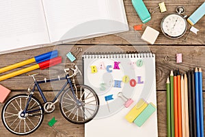 inscription of & x22;back to school& x22;, bicycle model, stopwatch, book, notepad and other stationery on brown wooden table