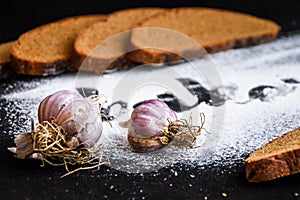 Inscription bakery on white wheat flour scattered Sliced rye bread with garlic on dark background