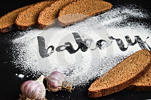 Inscription bakery on white wheat flour scattered Sliced rye bread with garlic on dark background