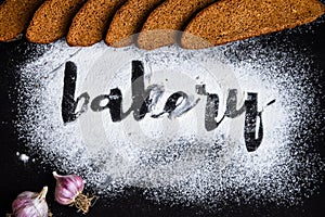 Inscription bakery on white wheat flour scattered Sliced rye bread with garlic on dark background