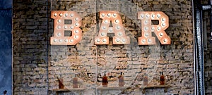 Inscription Bar of light bulbs against the wall of bricks