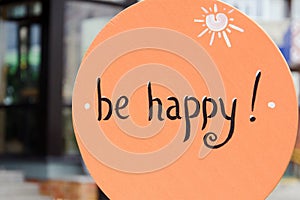 The inscription `be happy` on an orange wooden plaque