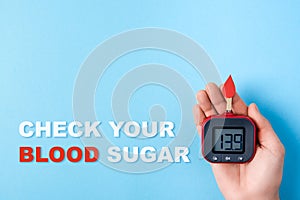 Inscription check your blood sugar,red blood drop,Blood glucose test strips,Glucose meter in man hand on blue background