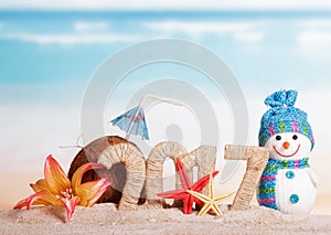 Inscription 2017, coconut, starfish, flower, snowman in sand against sea.