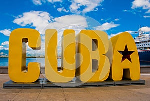 The inscription of the CUBA. Huge letters on the waterfront, against a blue sky with clouds in Santiago de Cuba.