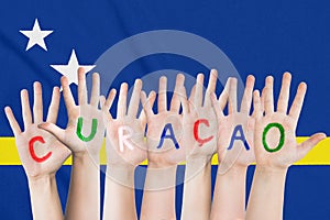 Inscription Curacao on the children`s hands against the background of a waving flag of the Curacao
