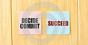 Inscription DECIDE COMMIT SUCCEED on pink and blue square sticky sticker on wooden wall