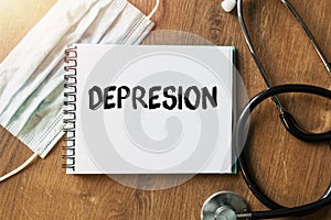 Inscription - DEPRESION. Written in a notepad to remind you of what`s important. Top view of the table along with a stethoscope