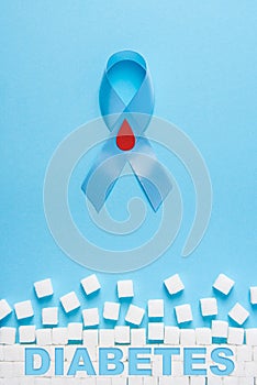 Inscription diabetes blue ribbon awareness with red blood drop and ruined wall made of sugar cubes on a blue background