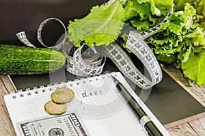 The inscription `diet` on a notebook, dollars, coins and vegetables on the table