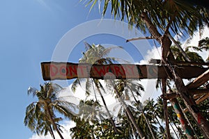 An inscription â€œDonâ€™t worryâ€ on the wooden abandoned hut on the palms tree and sky background.