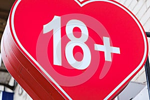 The inscription eighteen 18 plus on the background of a red heart on a store sign