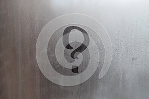 The inscription on glass, question mark concept. Question sign is painted on the surface of misted and wet window