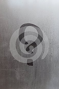 The inscription on glass, question mark concept. Question sign is painted on the surface of misted and wet window
