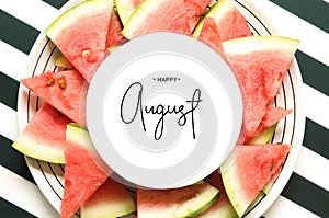 Inscription Happy August. Fresh red watermelon slice  in plate on striped background. Top view, Flat lay.