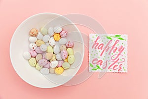 Inscription HAPPY EASTER letters candy chocolate eggs and jellybean sweets isolated on trendy pastel pink background. Simple