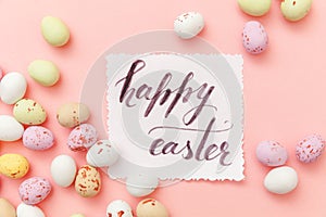 Inscription HAPPY EASTER letters candy chocolate eggs and jellybean sweets isolated on trendy pastel pink background. Simple