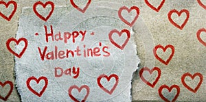 The inscription Happy Valentine`s Day in red pencil on piece of craft paper with many painted red hearts