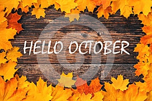 Inscription Hello October on a wooden background with a frame of orange maple leaves