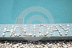 The inscription `holiday` is laid out by pebble on a pool side