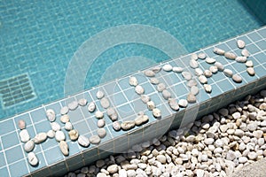 The inscription `holiday` is laid out by pebble on a pool side