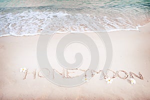 Inscription Honeymoon written on the sandy beach with ocean wave