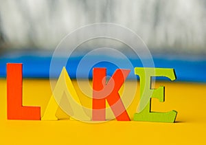 Inscription lake from multicolored bright wooden letters lie on a bright yellow background copy space. holiday vacation concept