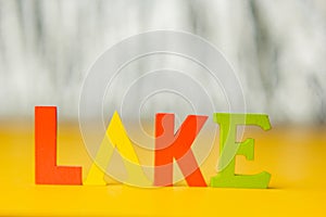 Inscription lake from multicolored bright wooden letters lie on a bright yellow background copy space. holiday vacation concept