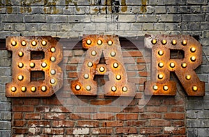 Inscription from large metal letters decorated with glowing light bulbs on the brick wall