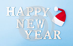 The inscription of the letters happy new year on a blue background. Little santa claus hat, new year holiday concept. Background,