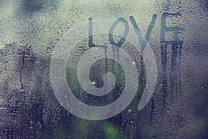 Inscription love on the wet glass rain