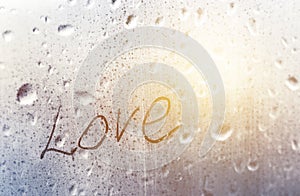 Inscription love on a wet window pane with raindrops