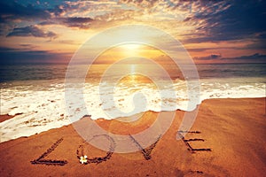 Inscription LOVE written on the sandy beach with ocean wave - sunset time.