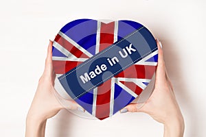 Inscription Made in UK, the flag of UK. Female hands holding a heart shaped box. White background. Place for text photo