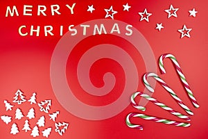 The Inscription Merry Christmas made of wooden letters, lying flat from above, isolated on a red background. Four candy canes visi