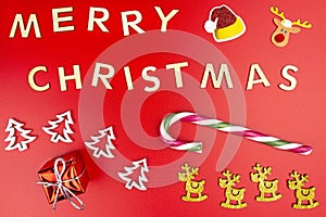 The Inscription Merry Christmas made of wooden letters, lying flat from above, isolated on a red background. Visible candy canes,