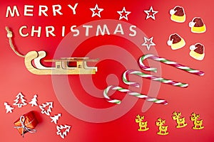 The Inscription Merry Christmas made of wooden letters, lying flat from above, isolated on a red background. Visible candy canes,