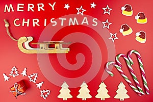 The Inscription Merry Christmas made of wooden letters, lying flat from above, isolated on a red background. Visible candy canes,