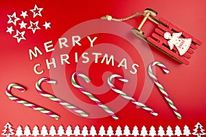 The Inscription Merry Christmas made of wooden letters, lying flat from above, isolated on a red background. Visible candy canes,